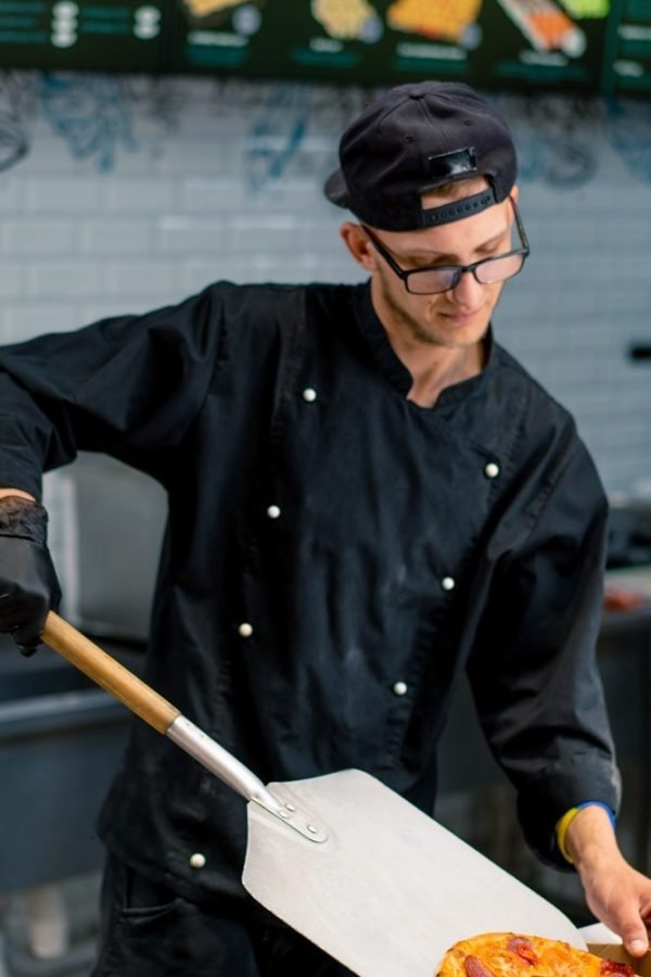 A pizzaiolo pulls a pizza from the oven with a pizza shovel and places it in a pizza box in the pizzeria kitchen